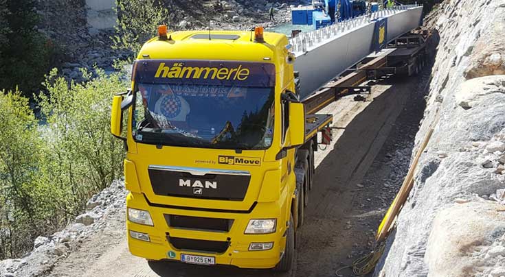 Mit ganz viel Fingerspitzengefühl: Bis zur Entladestelle sichert ein Bagger den Hämmerle-Zug mit dem Stahlkasten für eine neue Brücke. Foto: BigMove Mit ganz viel Fingerspitzengefühl: Bis zur Entladestelle sichert ein Bagger den Hämmerle-Zug mit dem Stahlkasten für eine neue Brücke. Foto: BigMove